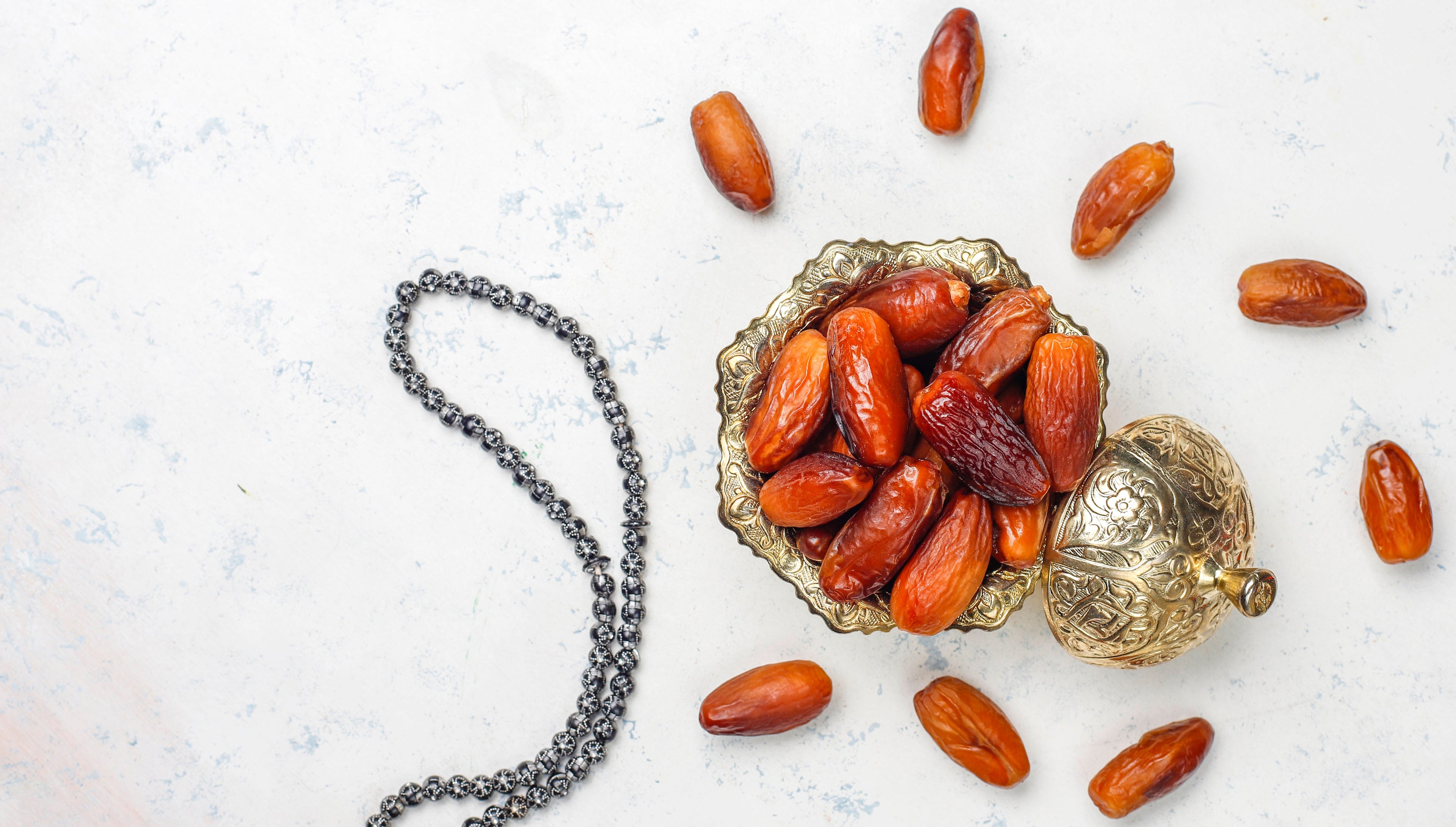 Dates in a brass bowl on white marble with prayer beads